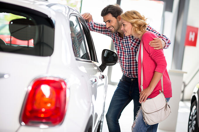 Young couple chooses to buy a car in car dealership saloon